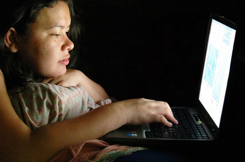 A girl learns on a laptop in a dark room